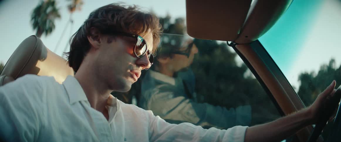 Young man wearing sunglasses driving a convertible vehicle