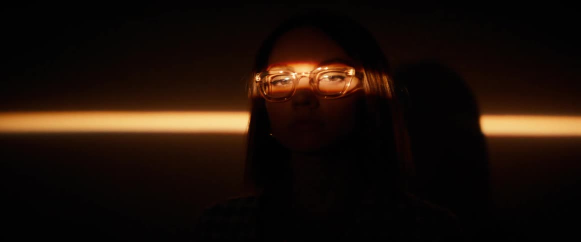 Face of a woman with a beam of light in her eyes while wearing glasses in a dark room