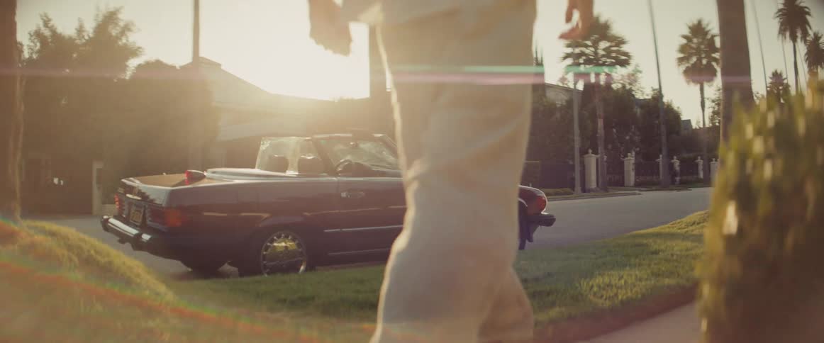 Legs of a man walking down the sidewalk towards a vintage convertible vehicle
