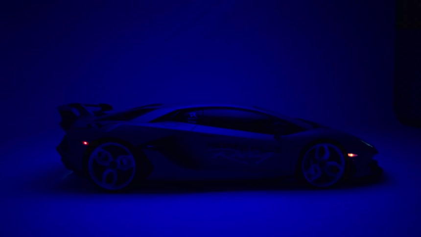 A lamborghini sports car sits in profile within a dark studio highlighted by flickering blue light