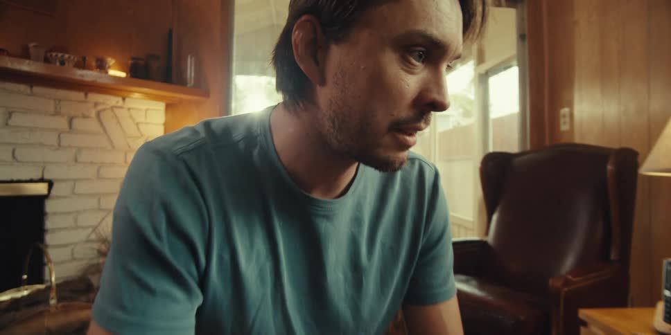 A young man sits with an elderly man in a cozy home on a sunny day engaged in conversation