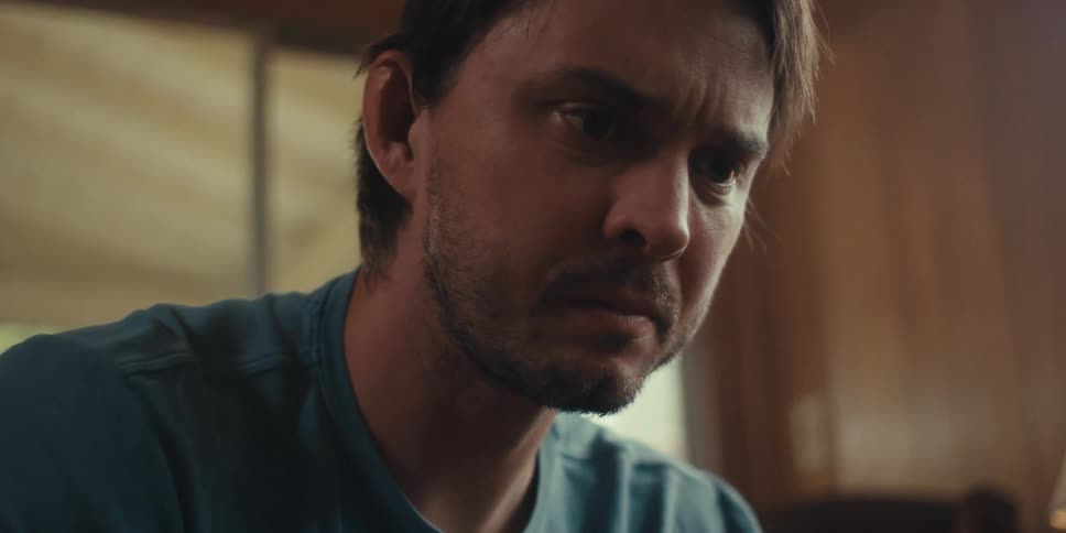 Close up of a young man wearing a blue shirt sitting on a living room foucsed on something