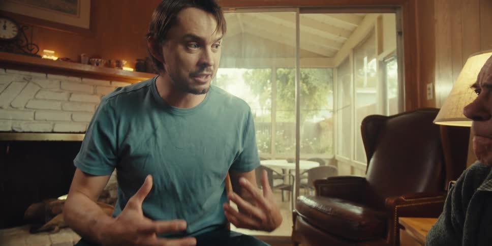 A young man sits with an elderly man in a cozy home on a sunny day offering an explanation