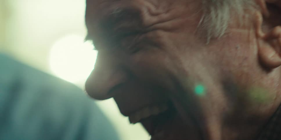 A closeup of an elderly man laughing and celebrating joyfully with someone beside him at home