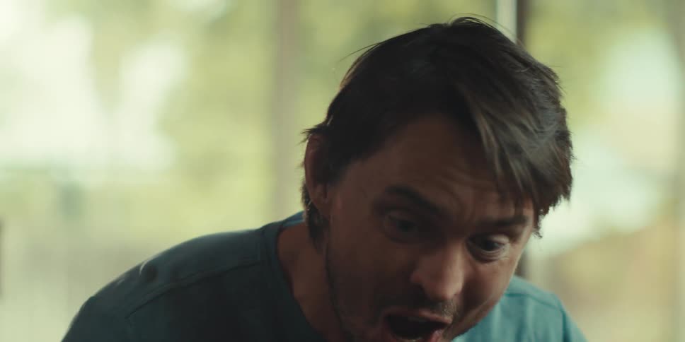 A young man in a blue shirt excitedly celebrates giving a high five to someone off screen in a sunny living room