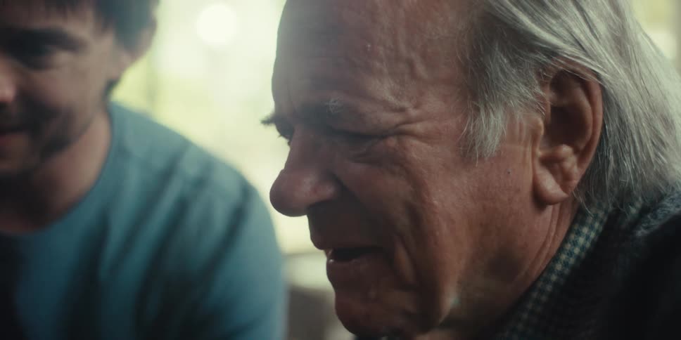 A close up of two men an older man with gray hair and a younger man seemingly engaged in a serious or contemplative conversation