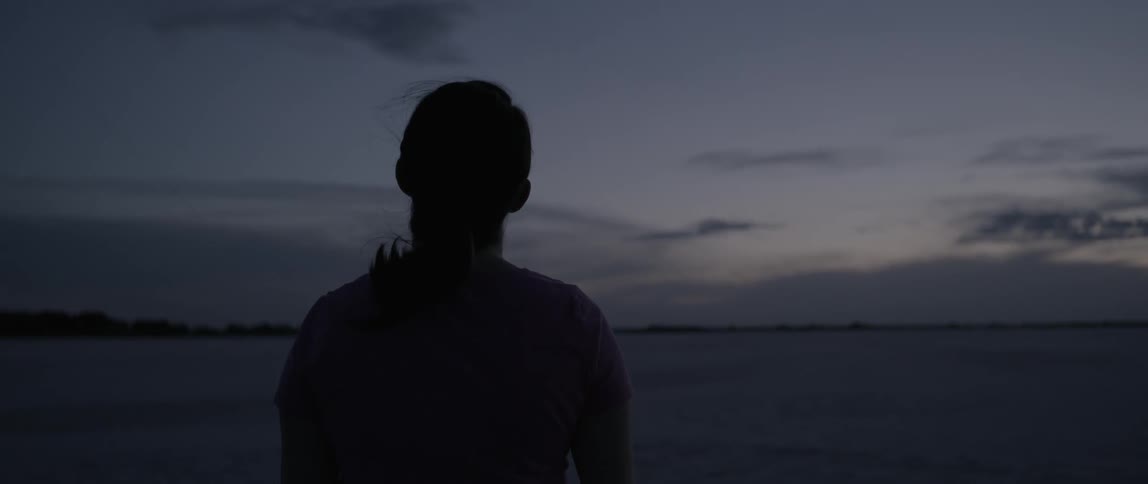 Ponytailed woman looking around and then looking upward towards the sky shortly after sunset