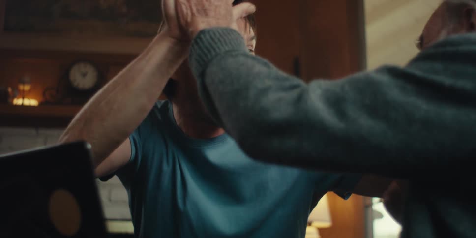 Elderly man and a young man clapping their hands together happily while watching something in front of a laptop
