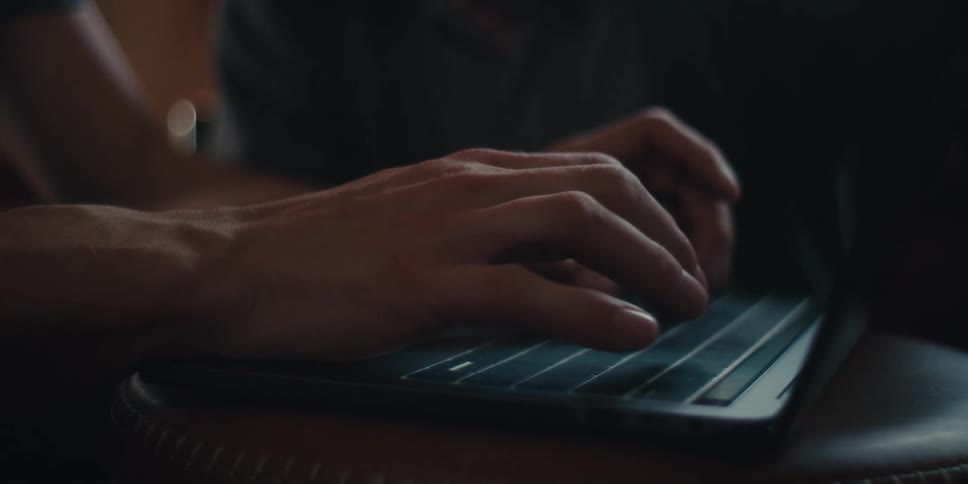 Pair of hands typing on a laptop and an elderly man in the background watching