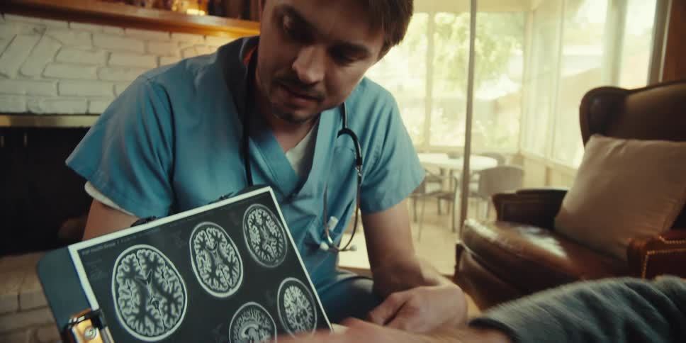 An elderly person points to a brain scan on an electronic tablet while meeting with a home health nurse