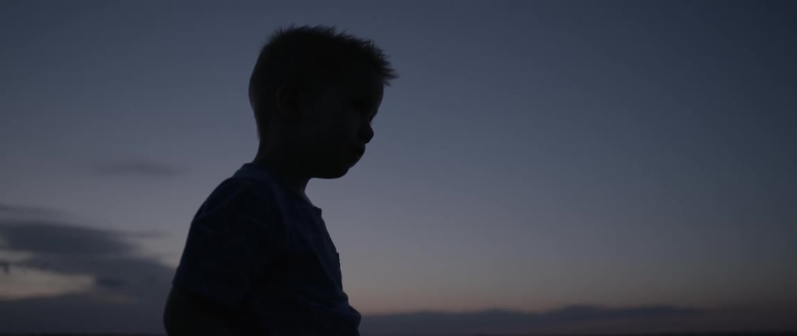 Silhouette of a child standing outside at night next to water