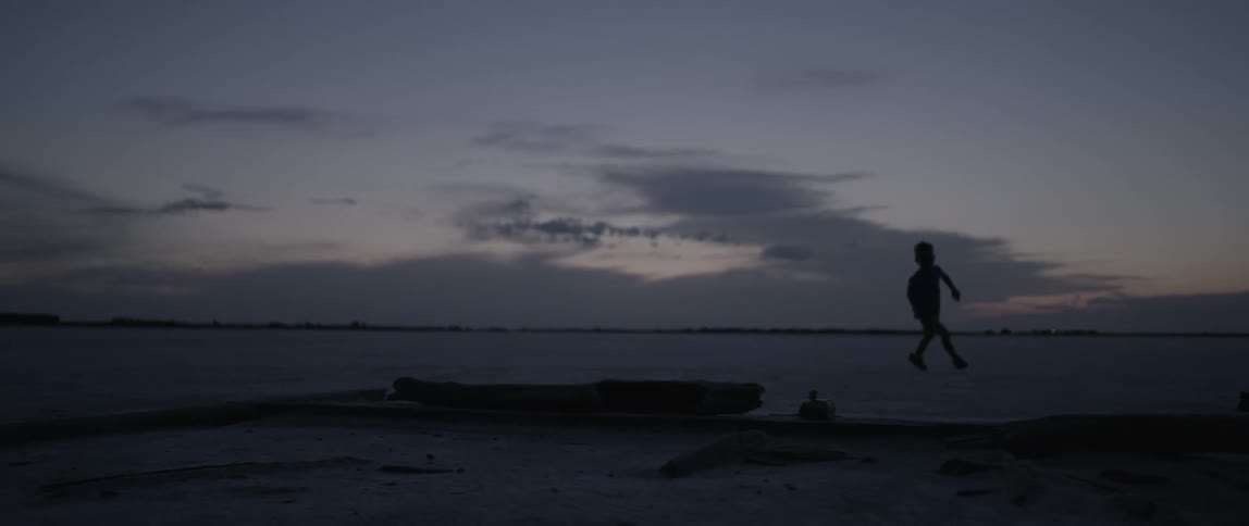 Little boy running and jumping over log on beach at dusk