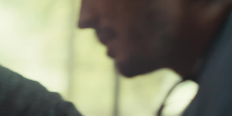 An older man with weathered features and graying hair engaged in conversation with a younger male nurse appearing to listen intently