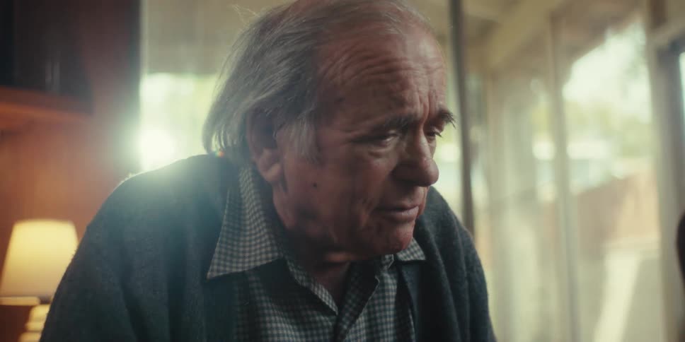 An elderly man gestures while talking to a younger man looking at a tablet the perspective slowly shifting to focus intently on the older mans expressive face