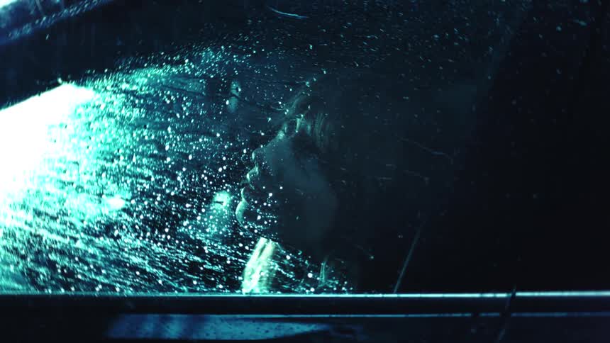 A woman sits in her car and looks out the window during a nighttime rainstorm