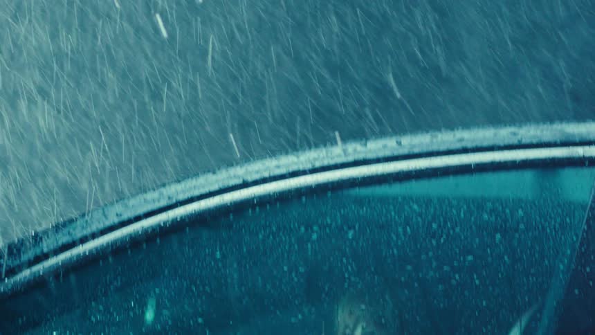 A woman sits in her car staring out the window while it rains really hard