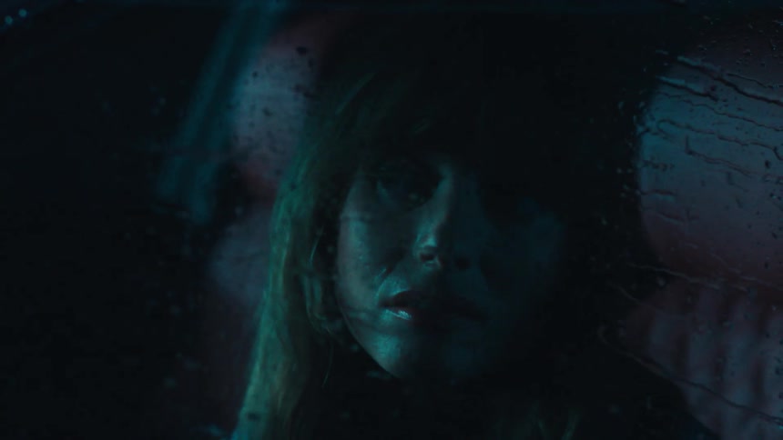 Portrait of a blonde woman inside a vehicle with rain flying out of the vehicle window