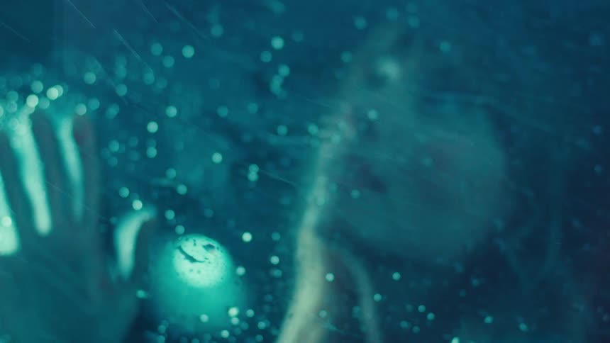 Woman looking out of car window at rain falling