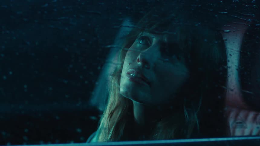 A footage of a lady in a car during a raining night