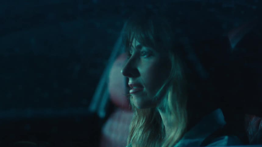 A closeup of a woman sitting in the drivers seat as heavy rain pours outside at night