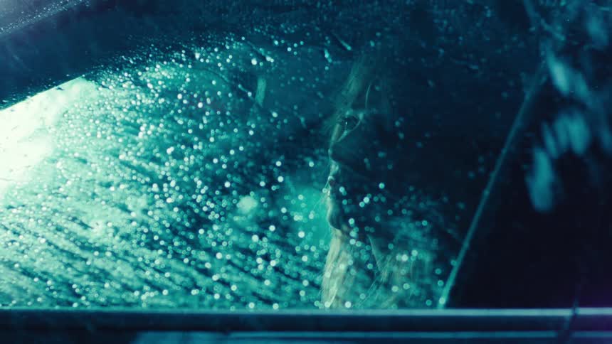 Blonde woman looking out the window while sitting in a car on a rainy night