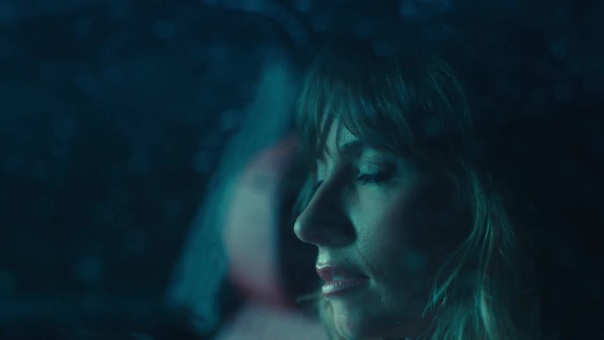 A woman sits in her car and looks out the window during a rainstorm at night