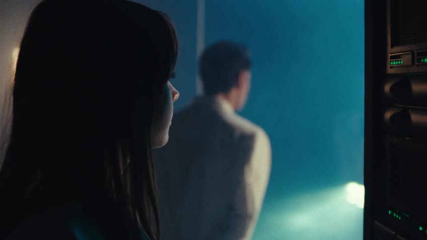A man and woman watch a storm through the window by the server racks