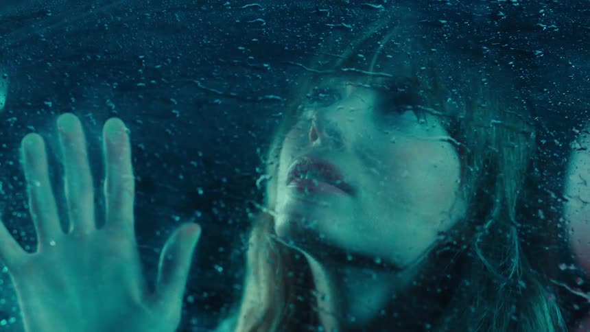A closeup of a woman sitting in the drivers seat gazing through a rolledup window as heavy rain pours outside at night