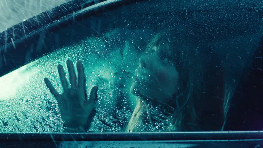 Portrait of a woman inside a car looking out the window at the rain falling