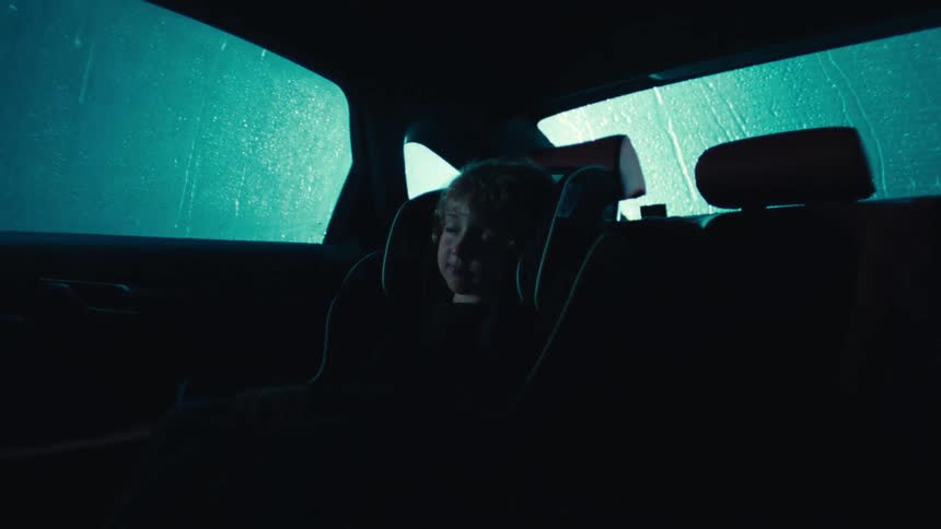 A young girl sleeps in a car seat during a rainstorm at night