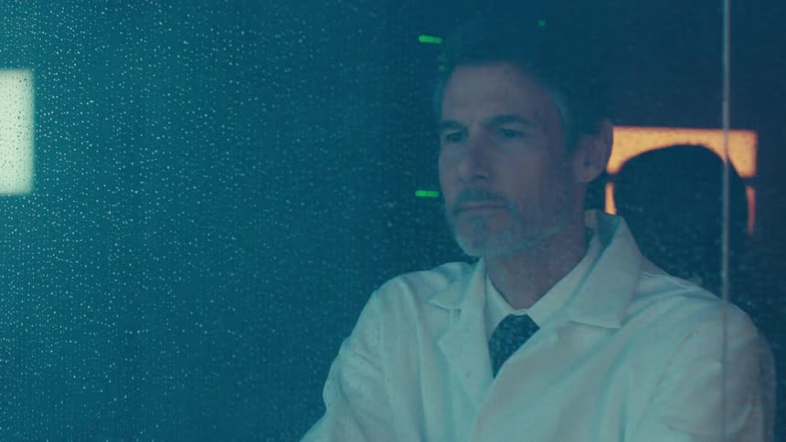 Scientist in the lab crossing his arms and observing an experiment with a woman in the background