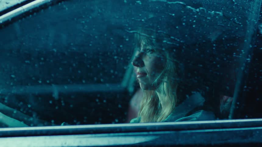 Blonde woman in the drivers seat of a vehicle with rain splashing down the vehicles windows