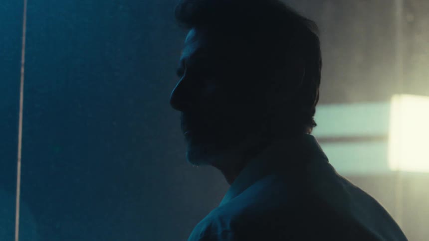 As the camera orbits a silhouetted man turns his head his face briefly illuminated by flashing lights
