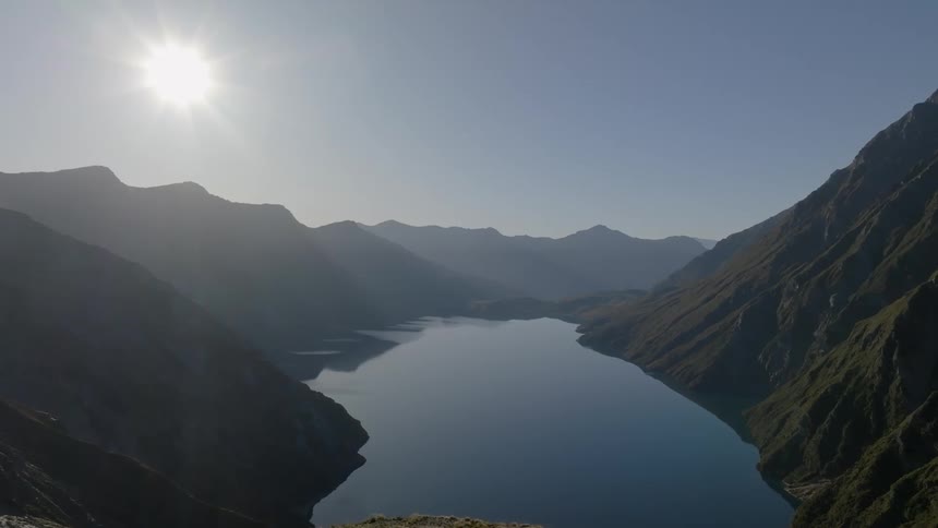 Natural landscape of a lake surrounded by mountains and the sun rising on the horizon