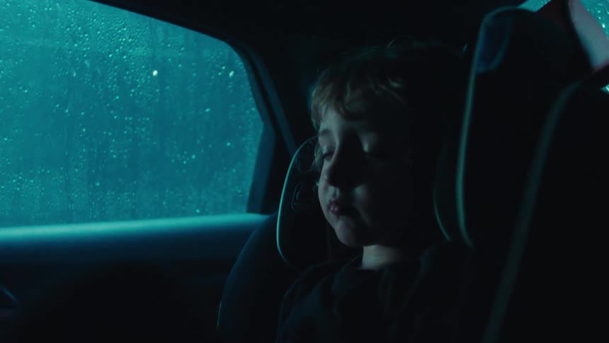 A little boy sits sleeping in the backseat of a car while a huge storm goes on outside