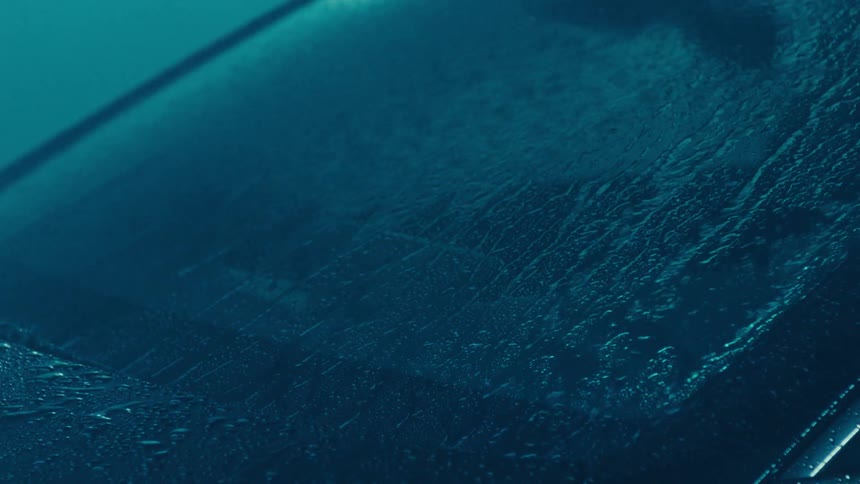 A close up of a car windshield with rain pouring down at night
