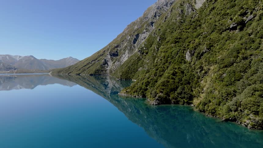 A serene turquoise lake reflecting the surrounding lush green mountains and a clear blue sky creating a stunning mirrored landscape