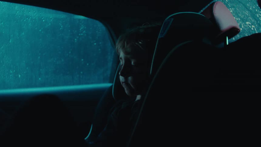 Little boy sleeping in a car seat in the back seat of a car while its raining