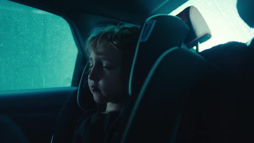 Child sleeping in a car seat in the back seat of a car while it is raining