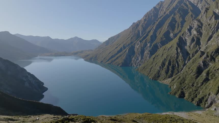 A lake amongst large mountains reflects the clear blue sky
