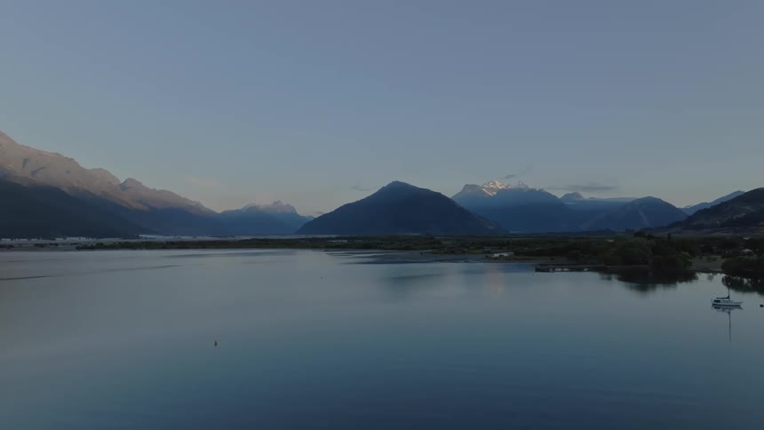 A tranquil lake reflects the silhouettes of distant jagged mountains under a dusky sky