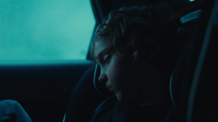 A young child sits in a car seat inside a dimly lit vehicle at night