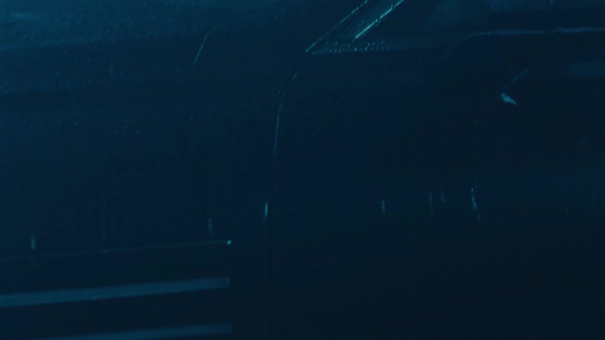 A camera pans up from a cars wet wheel in the dark to reveal a person sitting inside the vehicle through a rain streaked window