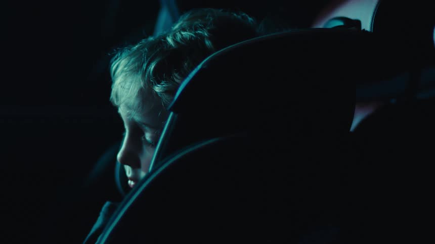 A young child sits in a car seat inside a dimly lit vehicle at night
