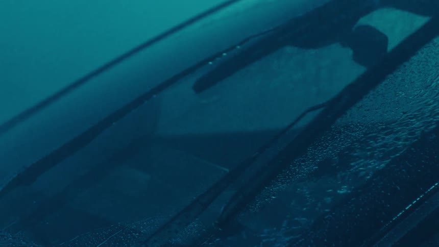 Rainwater flows down the windshield after the windshield wipers push it to the side during a rainstorm
