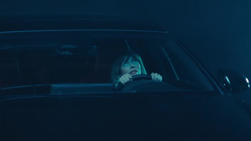 Female driver sitting in a parked car looks up at the sky while lightning lights up the night