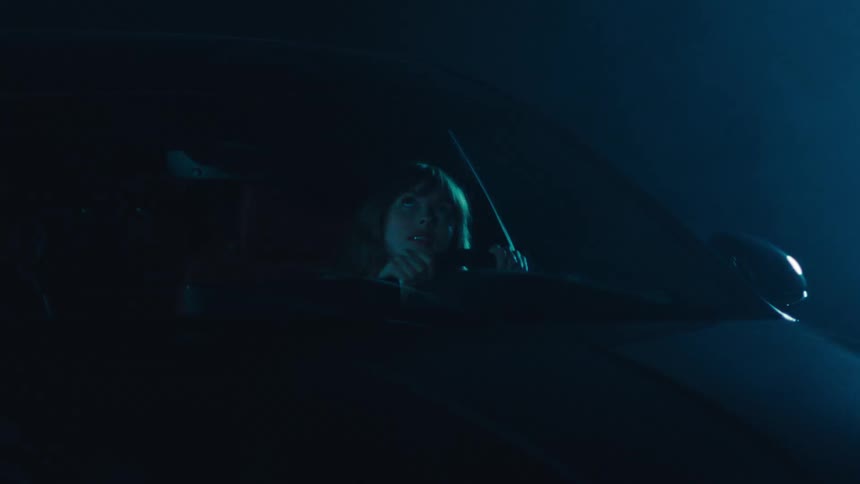 Woman inside a car with her hands on the steering wheel looking up at the windshield as thunder breaks
