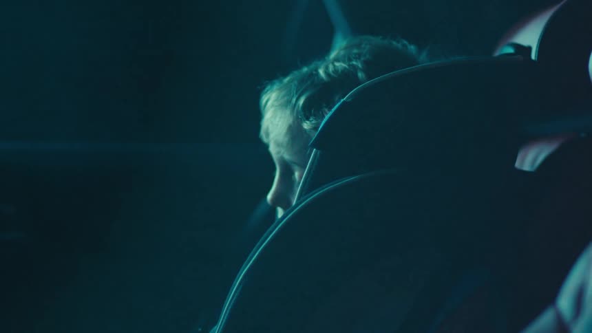 A young child sits in a car seat inside a dimly lit vehicle at night