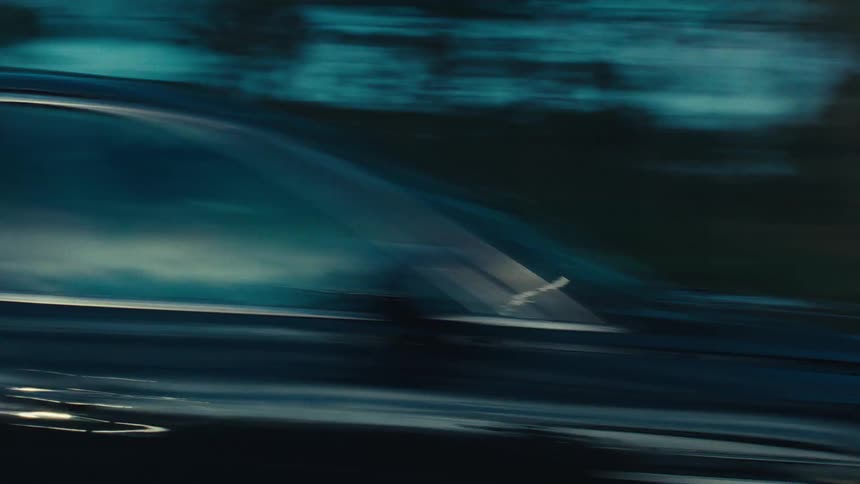 A black sedan travels along a road during dusk or dawn