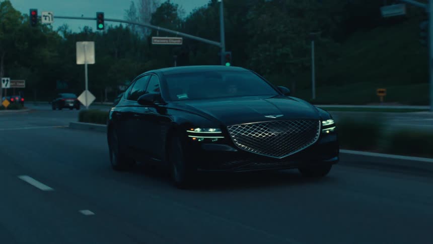 A black sedan travels along a road during dusk or dawn
